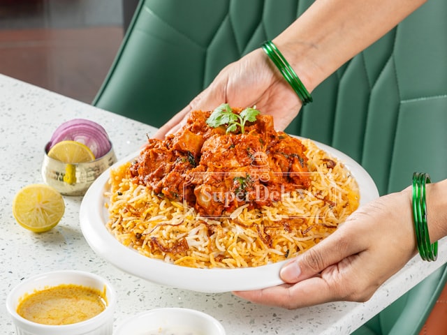 Chicken biryani being served with lemon and sauce