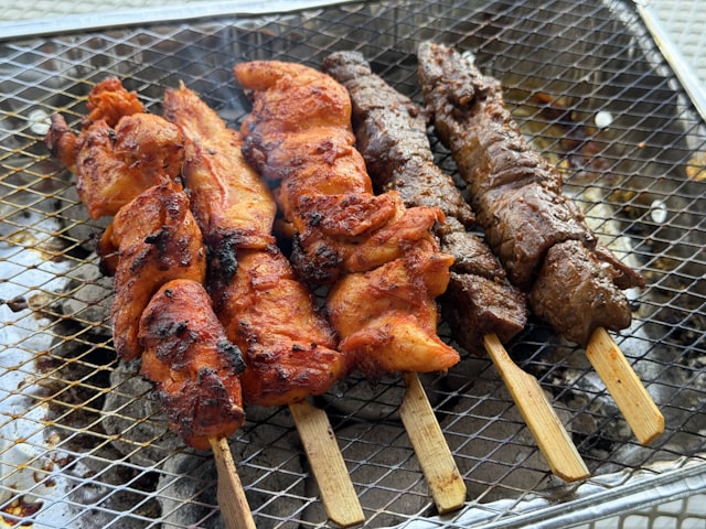 Chicken and beef skewers grilling over a metal grate