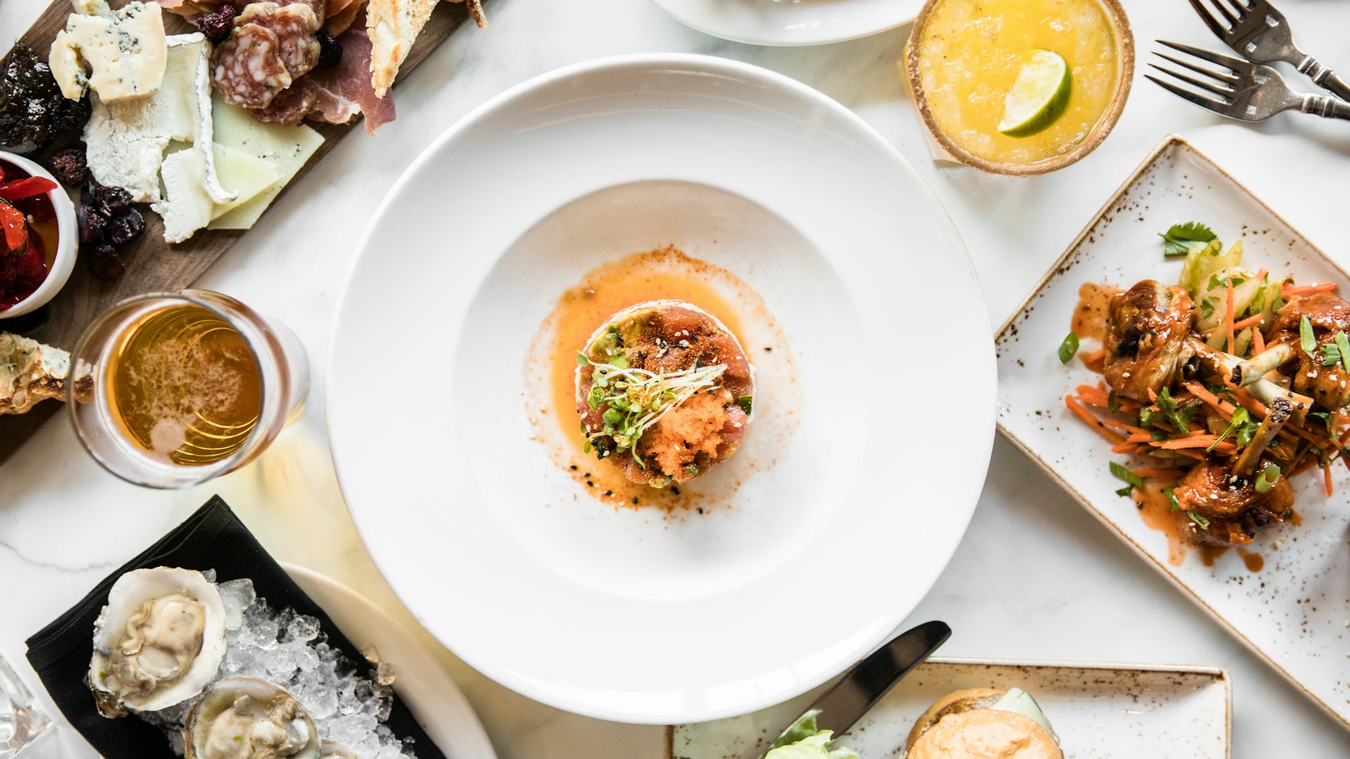 Overhead view of a sharing table laid with small plates, oysters and drinks